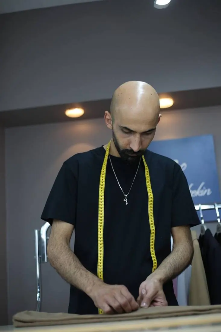 Terzi Gültekin, boynunda mezura ile kumaş üzerinde çalışırken